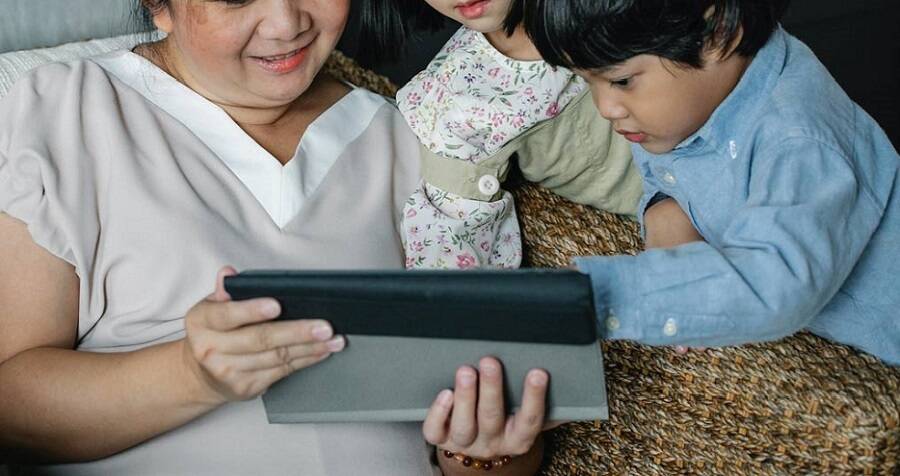 Une femme est assise avec deux enfants et regarde une tablette.
